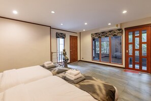 A hotel room with a large bed, a sitting area with a statue, and a sliding glass door leading to a balcony with plants. - Maan Tawan front beach Villa 12 (Choeng Thale)