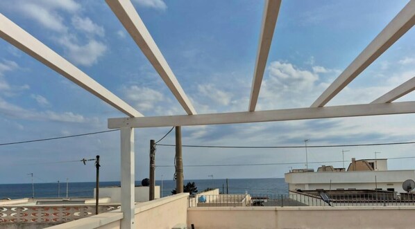 Ein Balkon mit Blick auf das Meer, weißen Tragebalken und einem klaren Himmel.