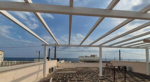Een terras op het dak met uitzicht op zee, een pergola en een gebouw op de achtergrond.