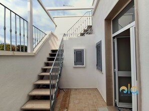 Una escalera que lleva a un piso superior, un vidrio corredero y un ventanal con contraventanas.