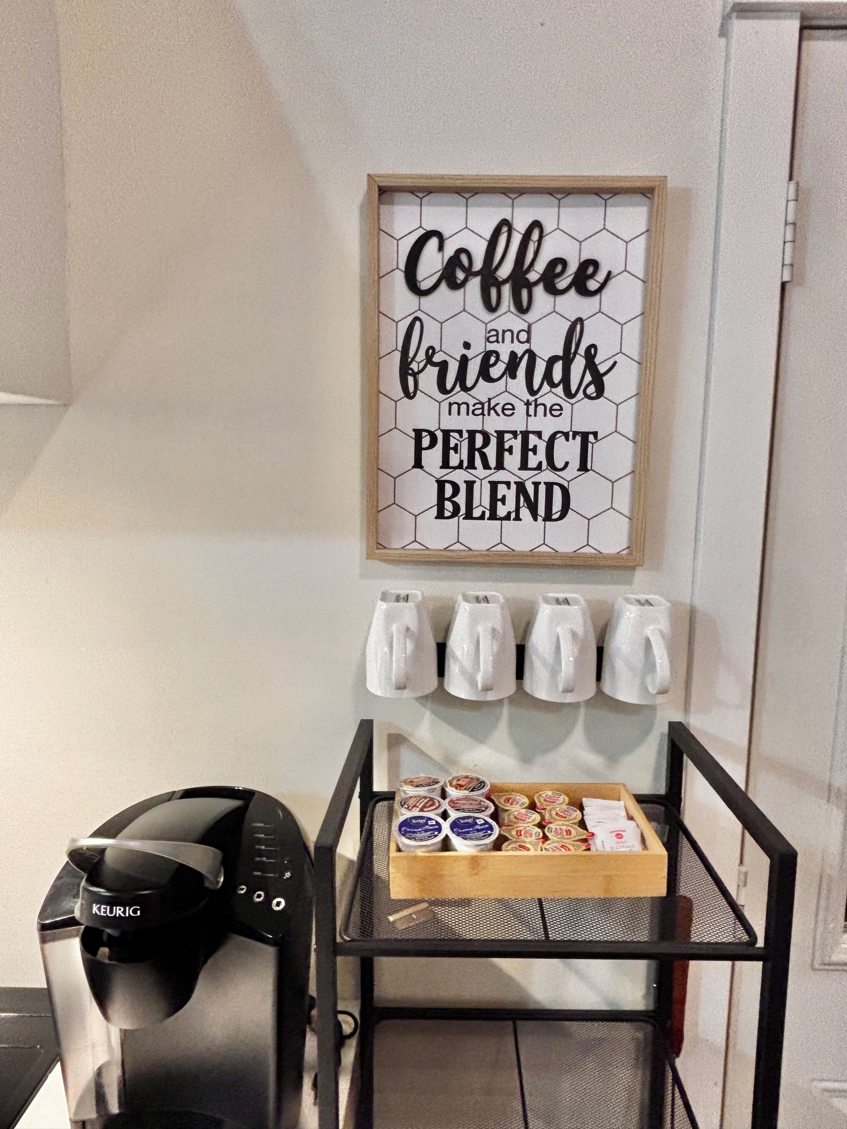 A coffee station with a Keurig machine, a tray of coffee pods, and a sign that reads 'Coffee and friends make the perfect blend.'