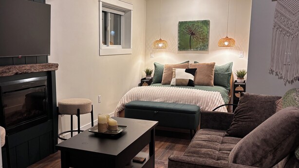 A compact living space with a sofa, a small table, a chair, a bed, a fireplace, and a wall-mounted artwork. - Rural Retreat. Private yard, fire pit. 3-30 mins to attractions & conveniences (Bothwell)