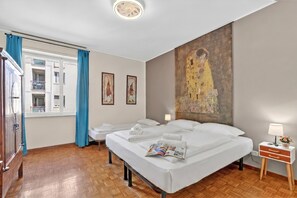A hotel room with two beds, a window with curtains, a painting on the wall, and a bedside table with a lamp. - Riva Dante Apartment, Riva del Garda, Italy (Riva del Garda)