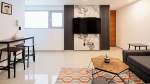 A modern living room with a flat-screen TV, a dining area with a table and chairs, and a sofa. - Massive rooftop terrace steps from everything (Mexico City)