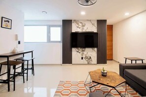 Ein modernes Wohnzimmer mit Flachbildfernseher, einem Essbereich mit Tisch und Stühlen sowie einer Couch.