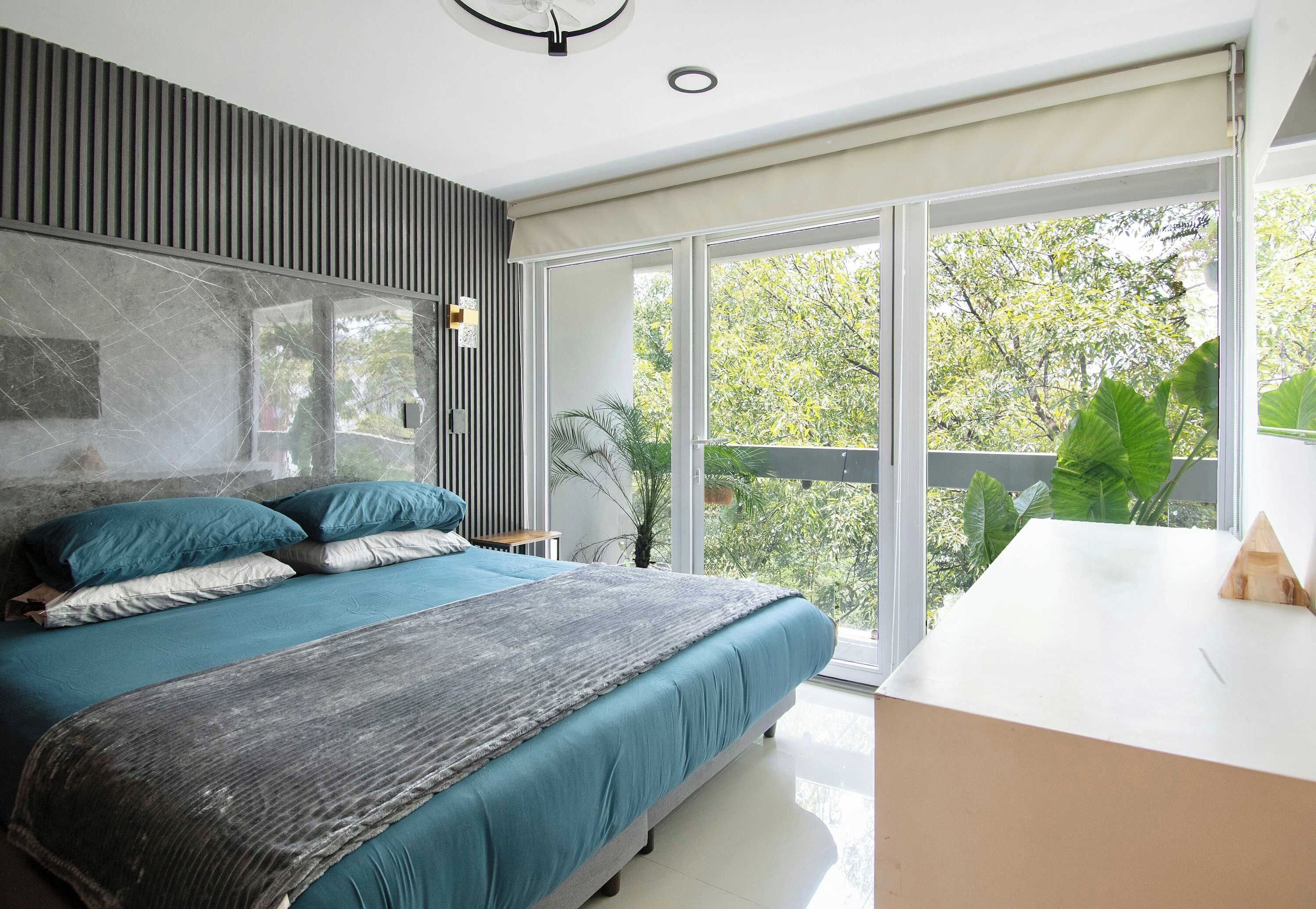 A modern bedroom with a large bed, a bedside table, and a view of greenery through a sliding glass door.