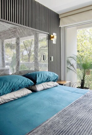 Ein modernes Schlafzimmer mit einem großen Bett, einem Fenster mit Blick auf Bäume und einer Zimmerpflanze.