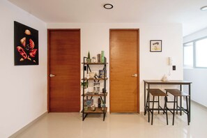 A room with a wooden door, a shelf with various items, a framed picture, and a table with chairs. - Massive rooftop terrace steps from everything (Mexico City)