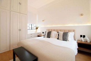 Una camera da letto con un letto grande, un'armadio bianco, un comodino e una panca.