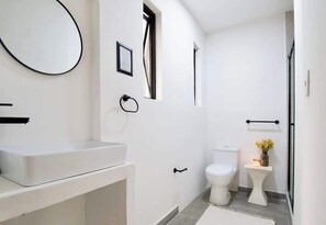 Une salle de bain moderne avec un lavabo, des toilettes et une zone de douche, le tout de couleur blanche.