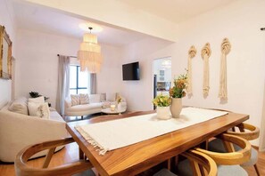 Un salon moderne avec une table à manger en bois, des canapés, un lustre et des décorations murales en macramé.