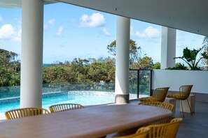 Ein moderner Außenbereich mit Sitzgelegenheiten, Blick auf einen Pool, weißen Säulen und gelben Stühlen.