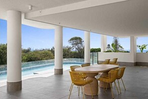 Ein überdachter Außenbereich mit Pool, einem runden Tisch und gelben Stühlen.