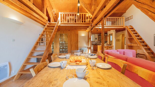 A wooden dining table with plates, cups, and a bread basket, surrounded by red and yellow upholstered seating. - Bel'Alp 24 Historical Residence Near Ski Lifts at Le Tour in Chamonix, Le Tour (Argentière), France (Le Tour (Argentière))
