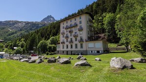 A multi-story building with balconies, surrounded by a grassy area with large rocks, and a mountainous backdrop. - Bel'Alp 24 Historical Residence Near Ski Lifts at Le Tour in Chamonix, Le Tour (Argentière), France (Le Tour (Argentière))