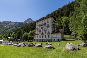 A multi-story building with balconies, surrounded by a grassy area with large rocks, and a mountainous backdrop. - Bel'Alp 24 Historical Residence Near Ski Lifts at Le Tour in Chamonix, Le Tour (Argentière), France (Le Tour (Argentière))