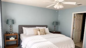 Ein Schlafzimmer mit einem Bett, zwei Nachttischen, einem Deckenventilator und einer Tür.