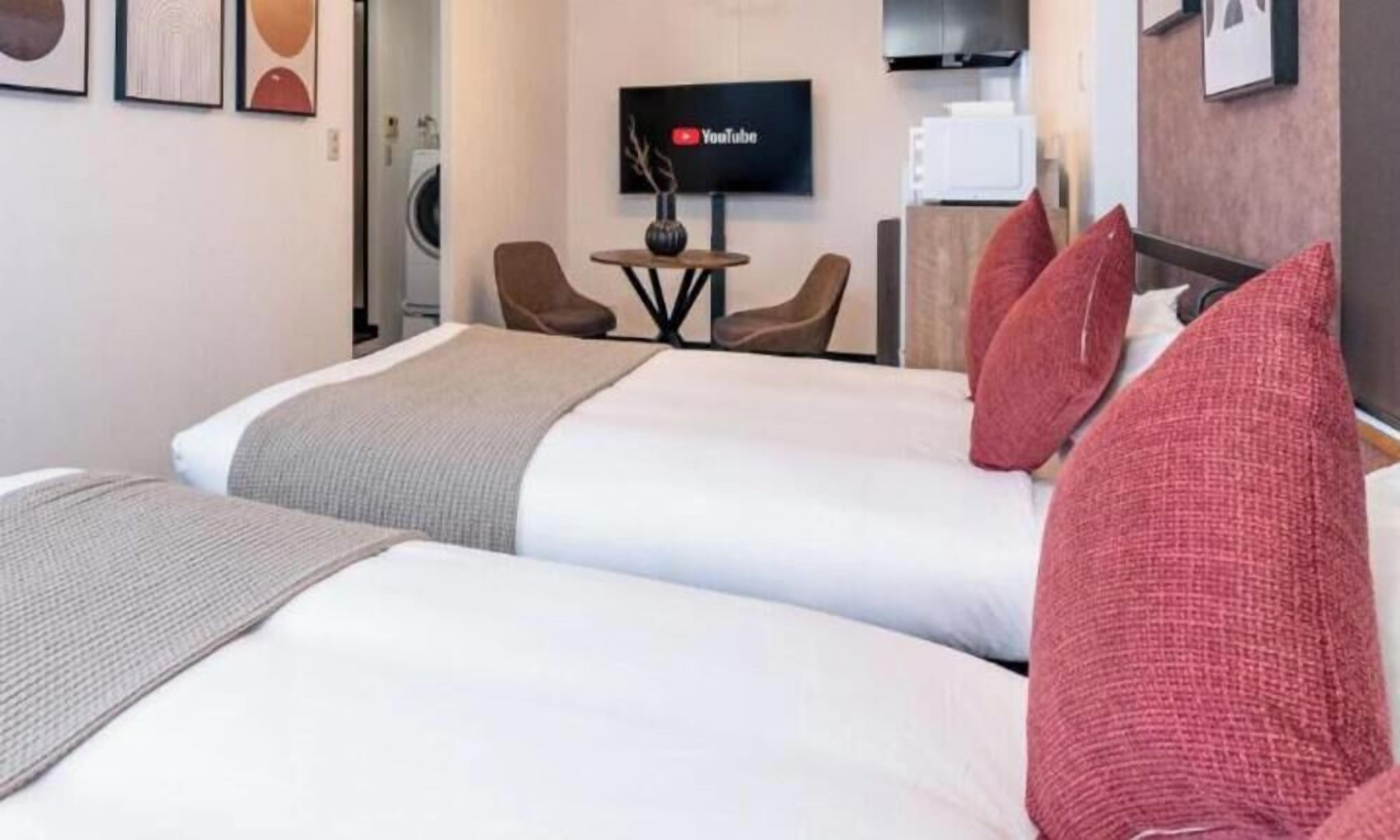 A hotel room with two beds, a TV, a small table, and chairs.