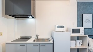 A modern kitchen with a built-in microwave, kettle, and coffee maker, a sink, and a stove. - Logement Tengachaya (Osaka, Nishinari ward, Tengachaya)