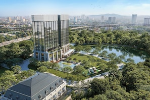 A modern building with a glass facade, surrounded by a park with a lake and walking paths. - Marqen Hotel (Jakarta)