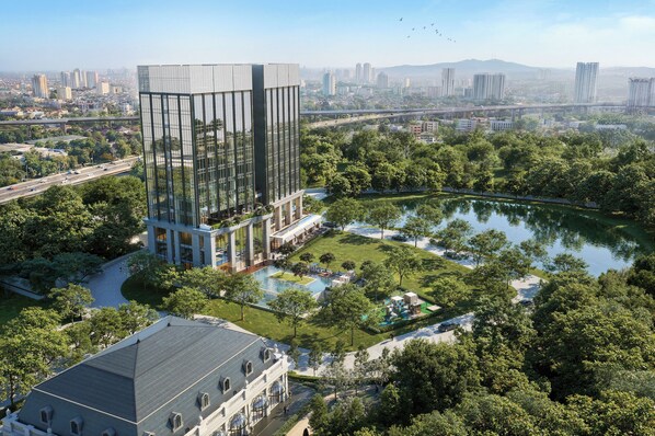 A modern building with a glass facade, surrounded by a park with a lake and walking paths. - Marqen Hotel (West Jakarta)