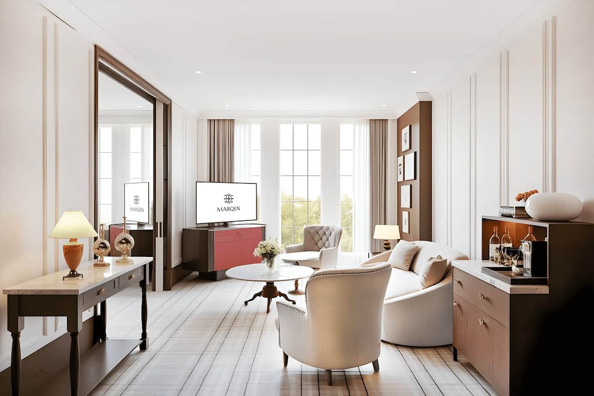 A modern hotel room with a large mirror, a flat-screen TV, a round coffee table, a sofa, and a cabinet with bottles.