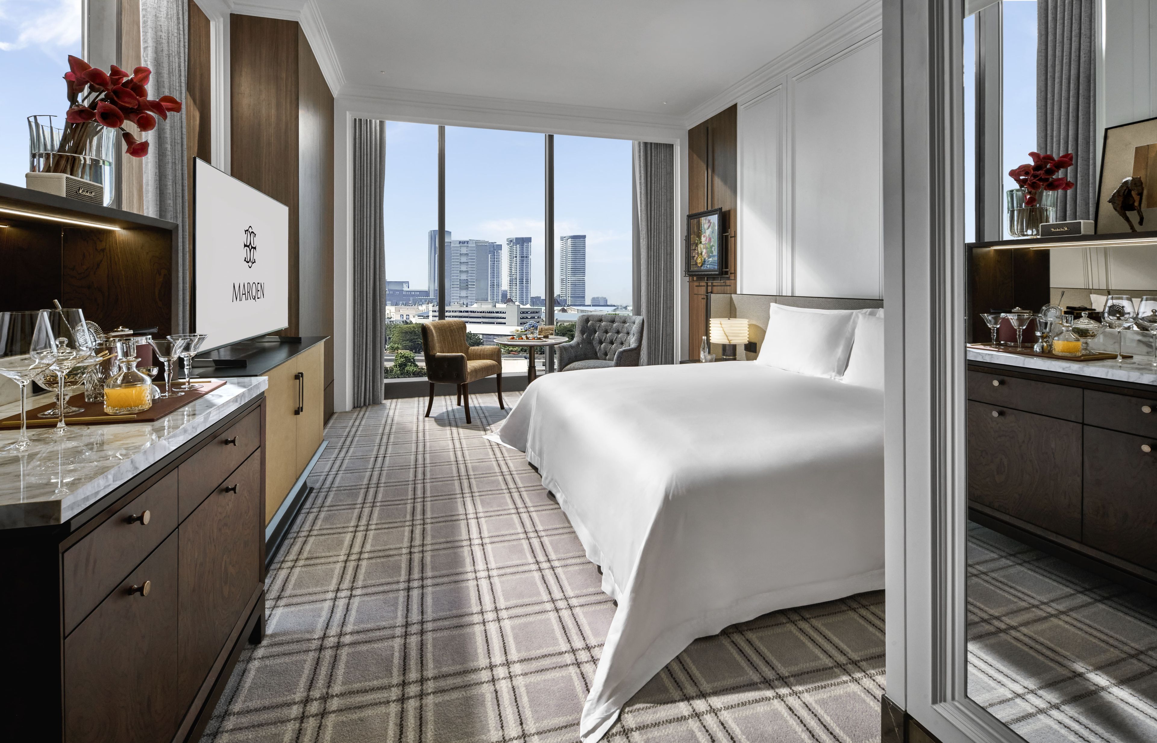 Una camera d'albergo con un letto, una scrivania con un minibar, vista sulla città e un'ampia finestra.
