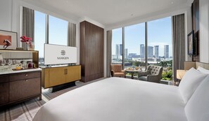A hotel room with a large bed, a TV, a minibar, a desk with a lamp, and a city view. - Marqen Hotel (Jakarta)