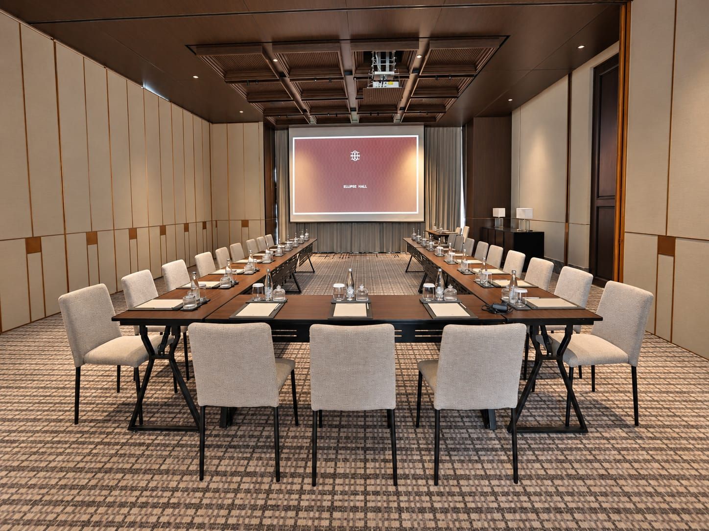 A conference room with a long table, multiple chairs, a projector screen, and a presentation screen.