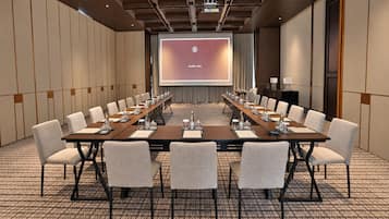 A conference room with a long table, multiple chairs, a projector screen, and a presentation screen.