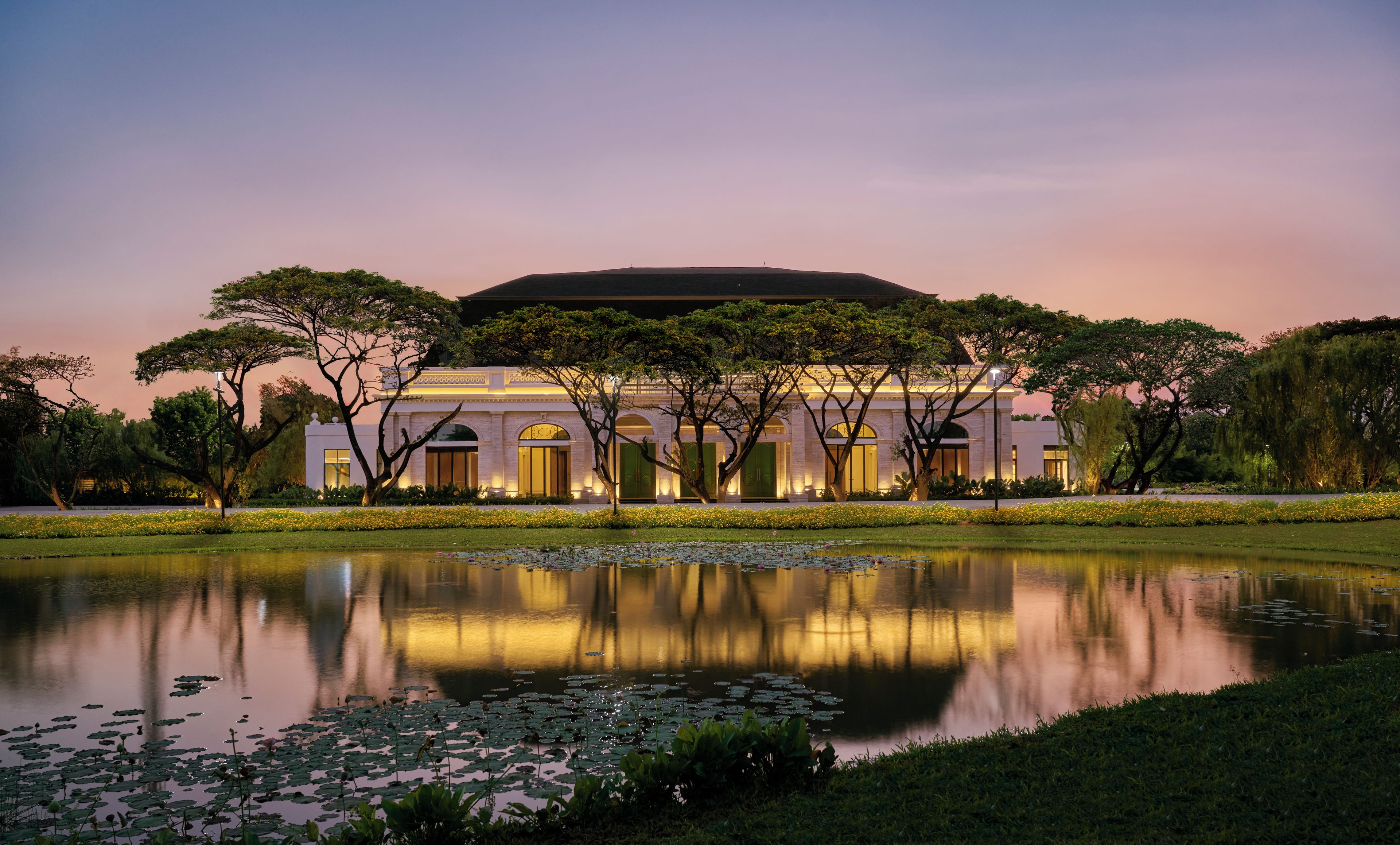 A large building with a reflective pond in front, surrounded by trees and a well-maintained lawn.