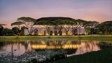 A large building with a reflective pond in front, surrounded by trees and a well-maintained lawn.