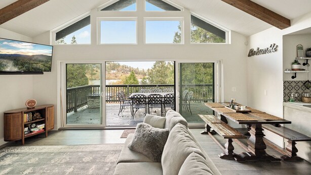 A spacious room with a high ceiling, a large sliding glass door leading to an outdoor deck, a sofa, a table, and a bench.
