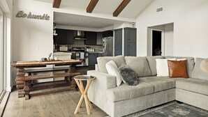 A modern living room with a sectional sofa, wooden dining table, and a kitchen in the background.