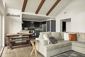 A modern living room with a sectional sofa, wooden dining table, and a kitchen in the background. - PREMIER 4BR LAKEFRONT HOME + BEST VIEWS + GENERATOR + EASY ACCESS TO LAKE (Crestline)