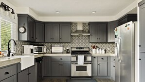 A modern kitchen with grey cabinets, stainless steel appliances, and patterned backsplash.