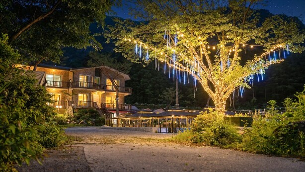 A multi-story building with balconies, a covered outdoor seating area, and a tree decorated with lights. - Pocheon New Dream Pension (Pocheon)