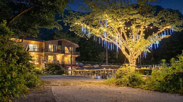 A multi-story building with balconies, a covered outdoor seating area, and a tree decorated with lights.