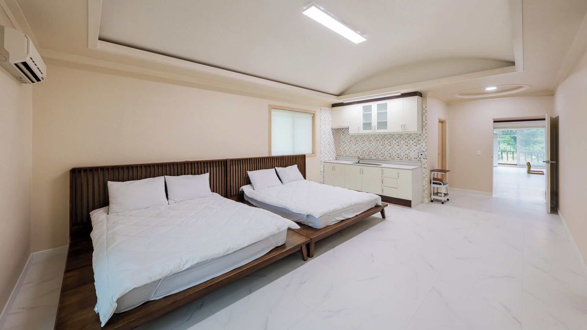 Ein modernes Schlafzimmer mit zwei Betten, einer Küchenzeile und Blick ins Freie.