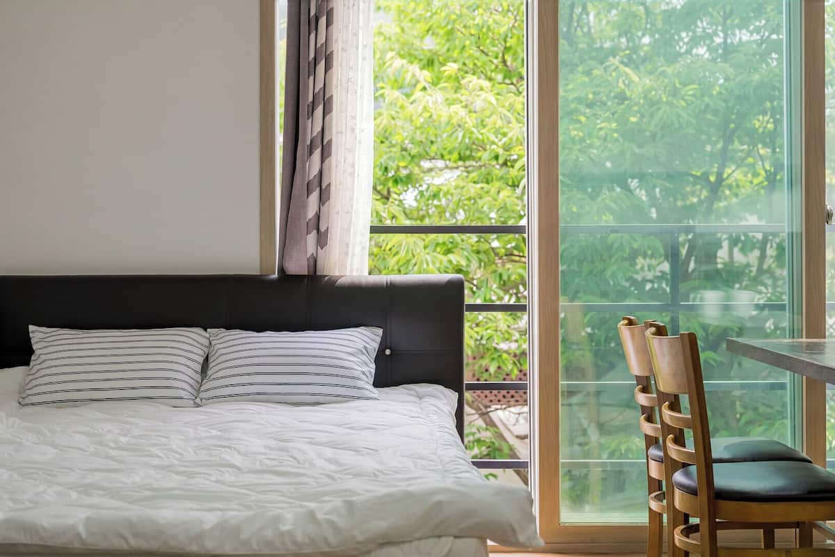 Un dormitorio con cama, una ventana con vistas a la vegetación y una mesa con sillas.