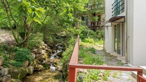 A serene garden with a small stream, a stone pathway, and a building with large windows. - Pocheon New Dream Pension (Pocheon)