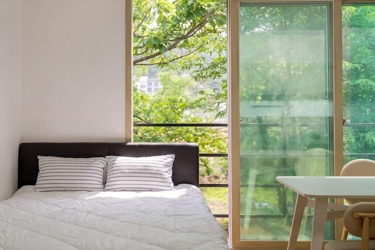Un dormitorio con cama, dos almohadas, una ventana y vistas a zonas verdes.