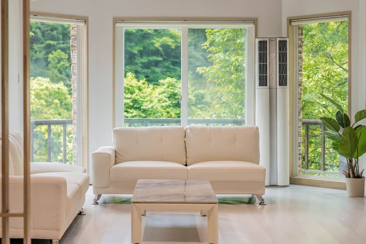 Una sala de estar moderna con un sofá color beige, una mesita y grandes ventanales con vistas a zonas verdes.