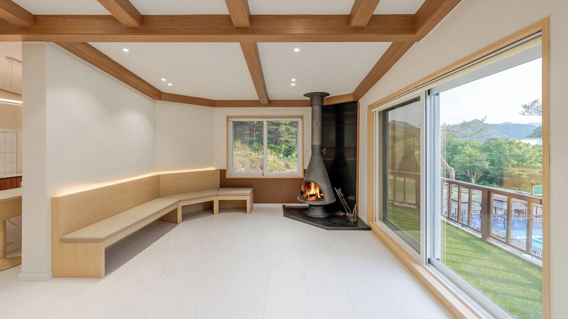 Un interior moderno con chimenea, asientos en banco de madera, ventanas amplias y vistas a zonas verdes.