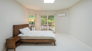 A bedroom with a bed, wooden nightstand, and a view of greenery through a sliding door.