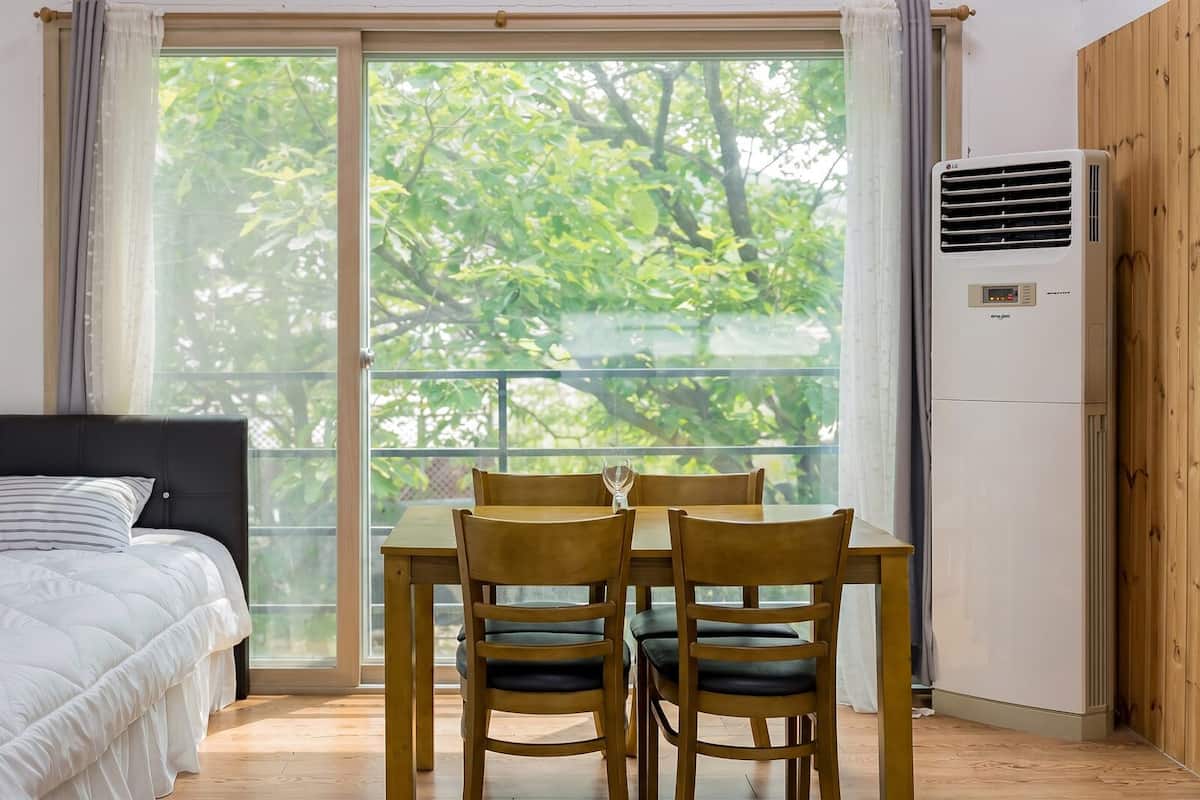 Un dormitorio con cama, una mesa con sillas y una ventana con vista a árboles.