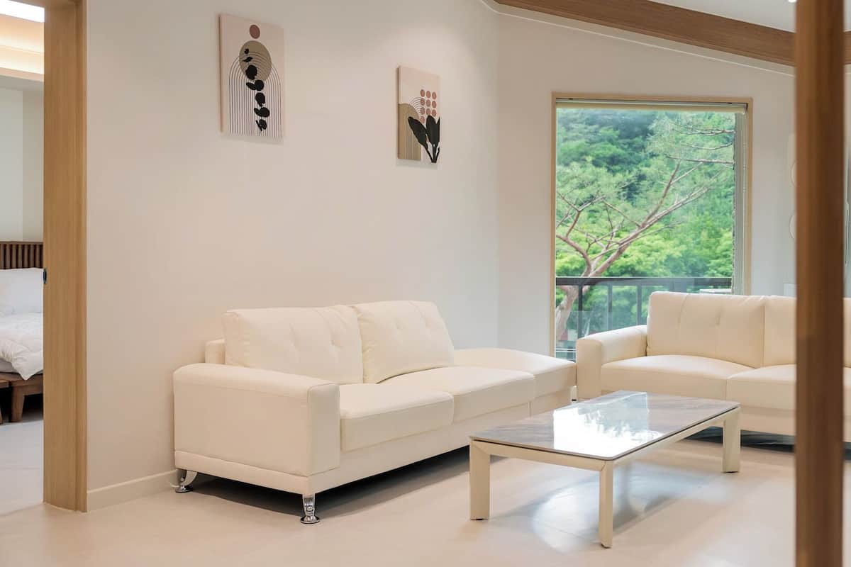 Una sala de estar moderna con dos sofás blancos, una mesa de centro de vidrio y obras de arte en las paredes.