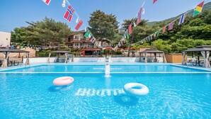 A swimming pool with flags, lounge chairs, and a building in the background. - Pocheon New Dream Pension (Pocheon)