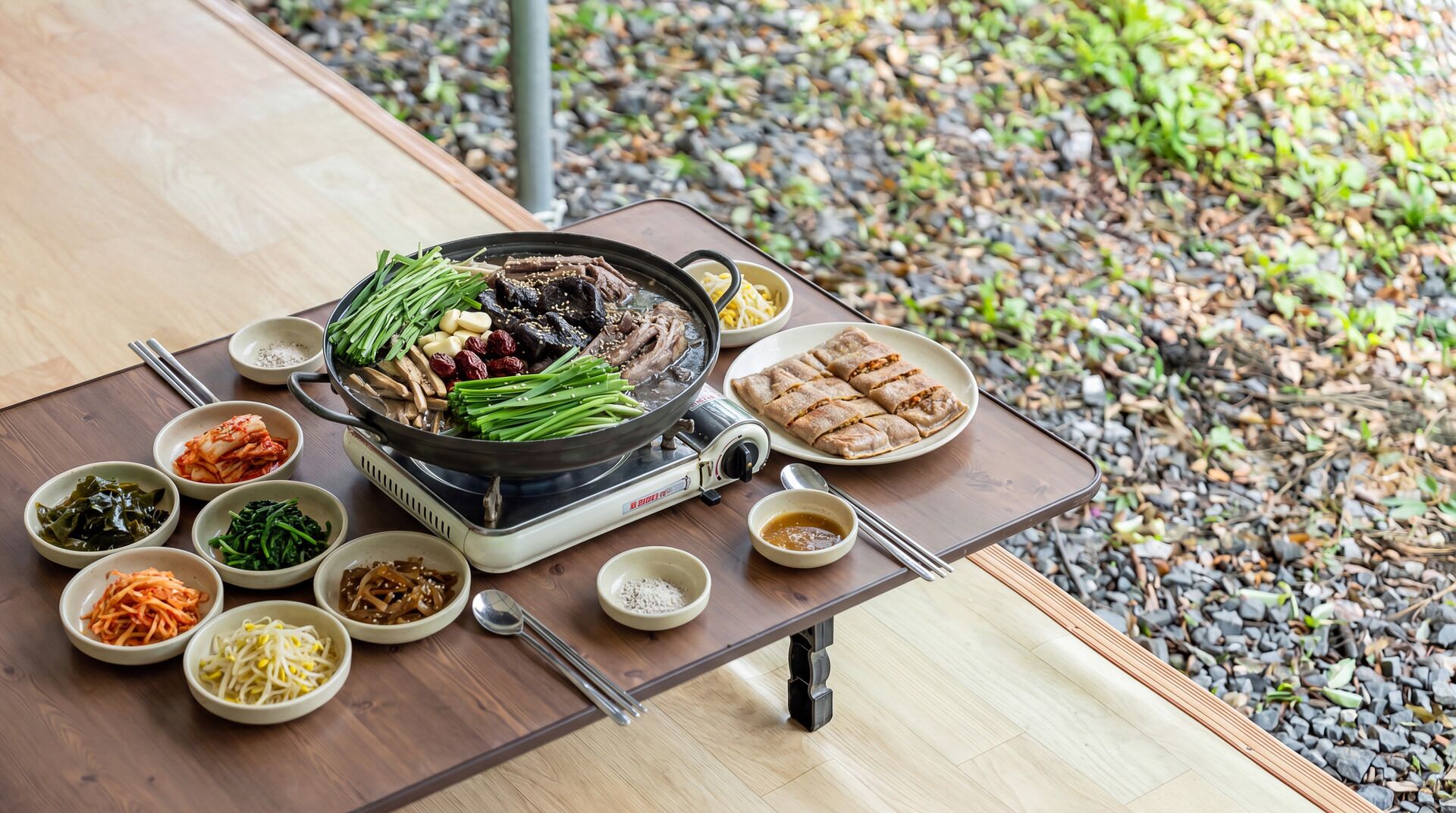 A table with a hot pot, various side dishes, and a portable grill.