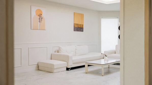 A modern living room with a white sofa, a coffee table, and two artworks on the wall.